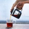 Main tenant la Cafetiere piston HARIO 300ml et qui verse du café dans une tasse transparente